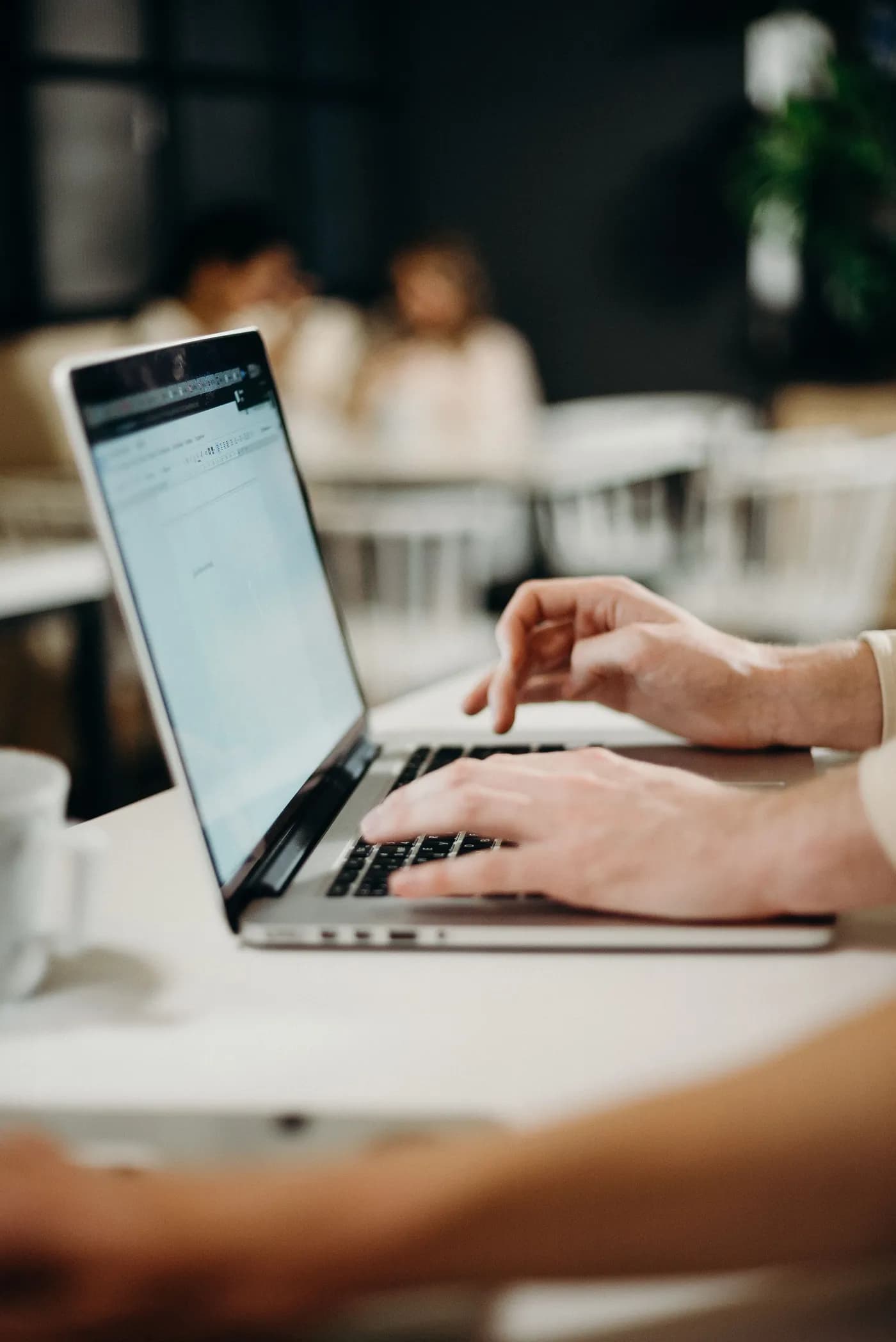 Hands typing a message on a laptop at a cafe table